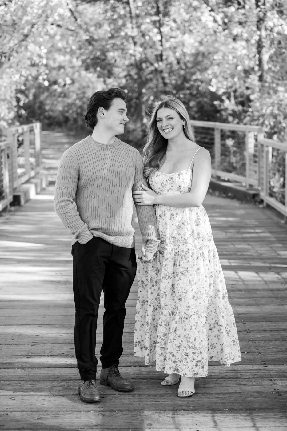 Black-and-white photo of a couple holding hands on a wooden bridge