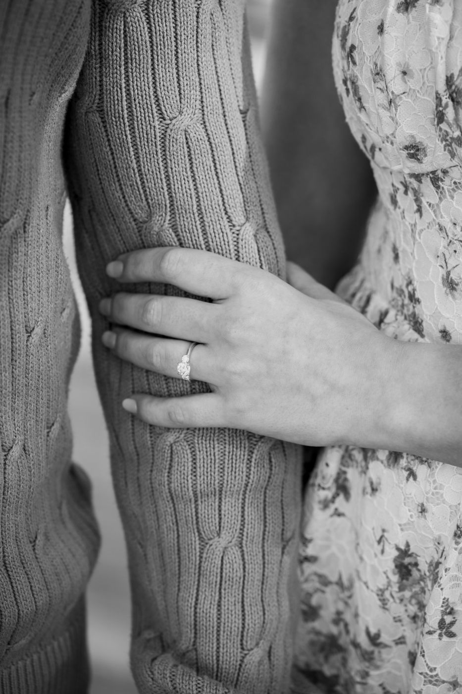 Black-and-white close-up of an engagement ring on a hand resting on a knit sweater