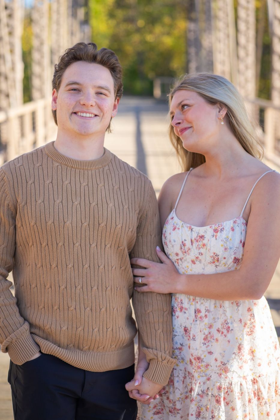 Engaged couple smiling on a wooden bridge in autumn