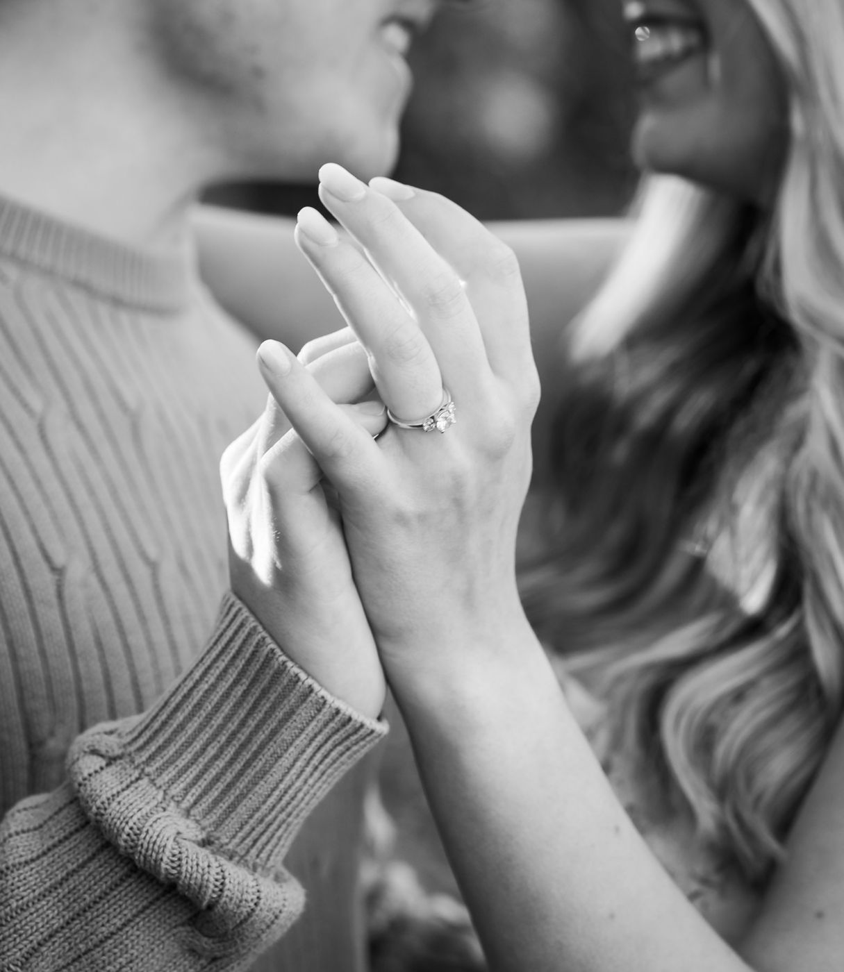 Black-and-white close-up of two clasped hands, engagement ring visible