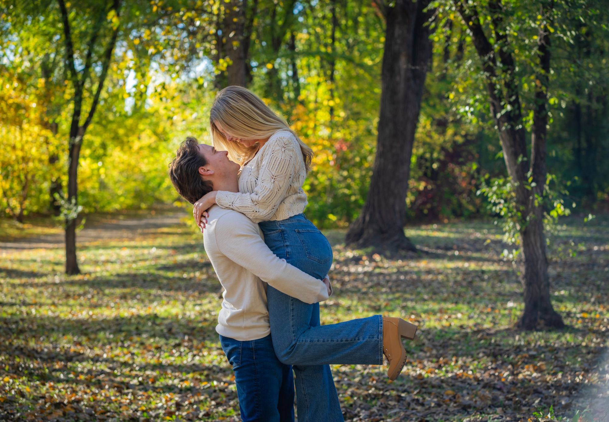 Couple embracing as he lifts her in golden fall woods, engagement session