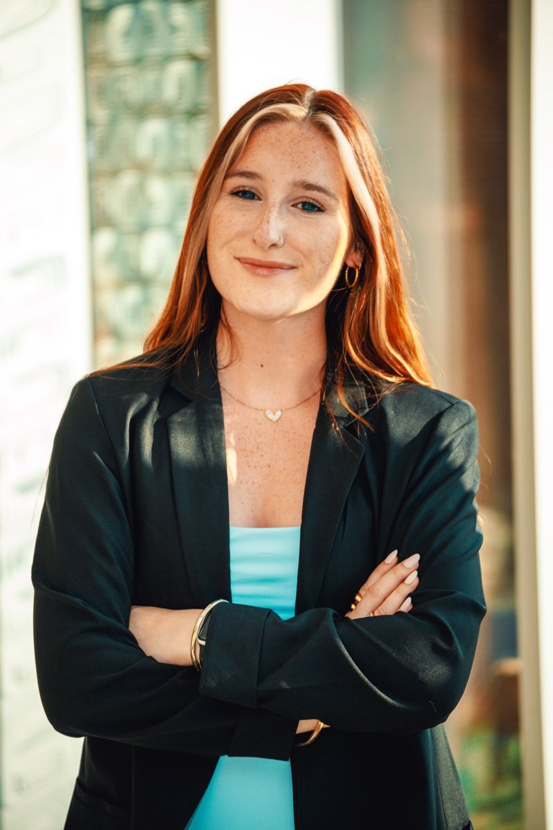 Professional headshot of a woman in a black blazer with arms crossed, smiling in warm natural light