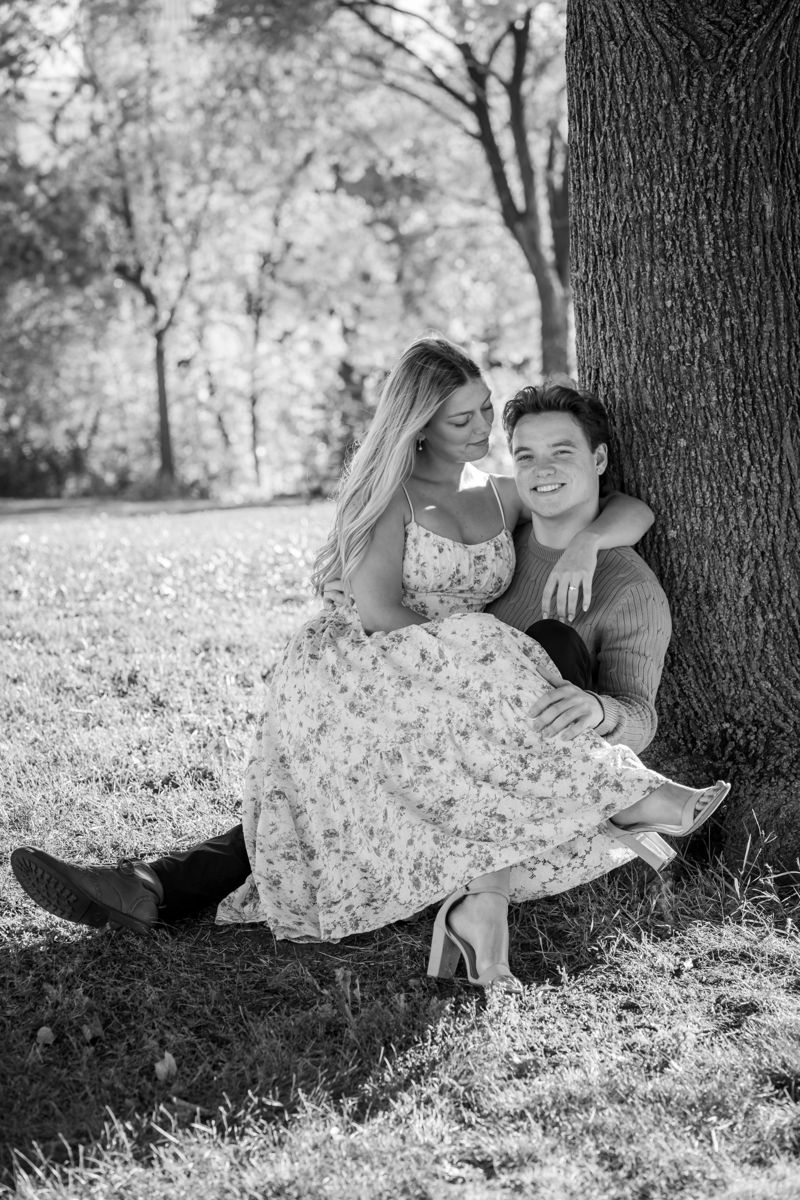Engaged couple cuddled together under a tree in black and white