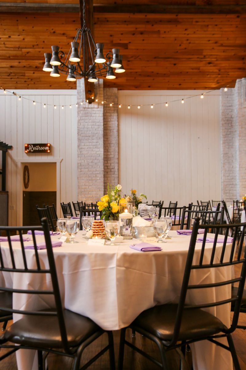 Reception table with candles and yellow flowers under a wood-beamed ceiling